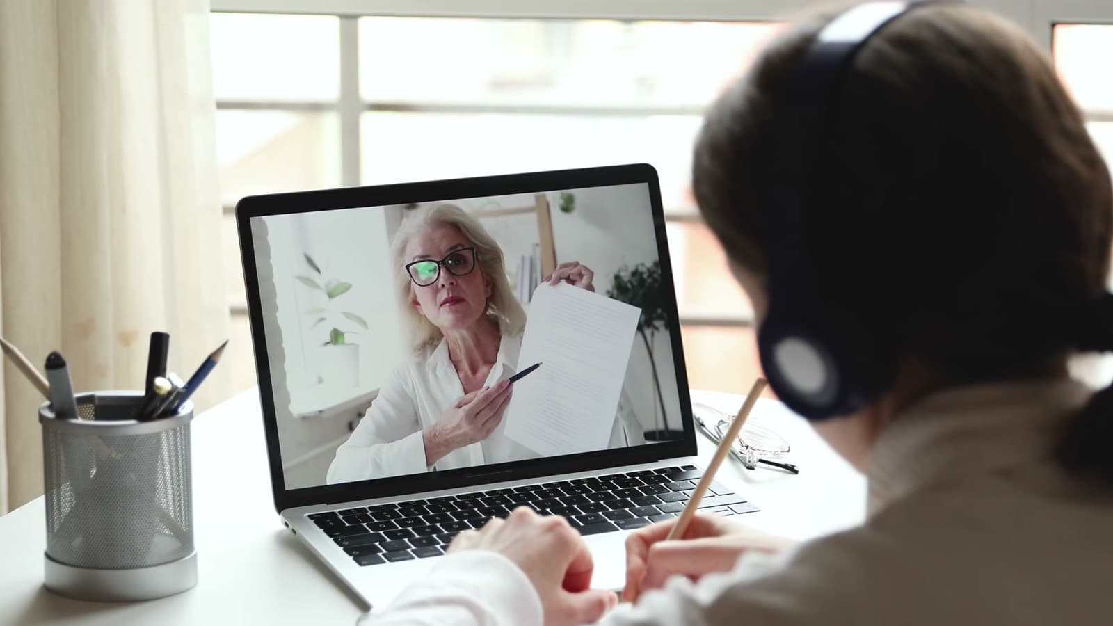 A student in headphones listening to her tutor explain a topic on screen