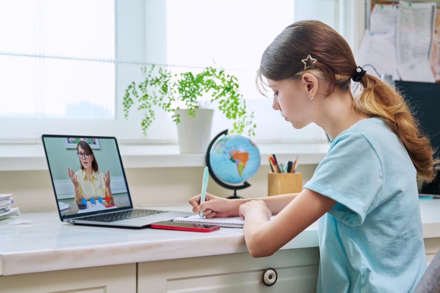 A student writing notes at her desk during a live online lesson
