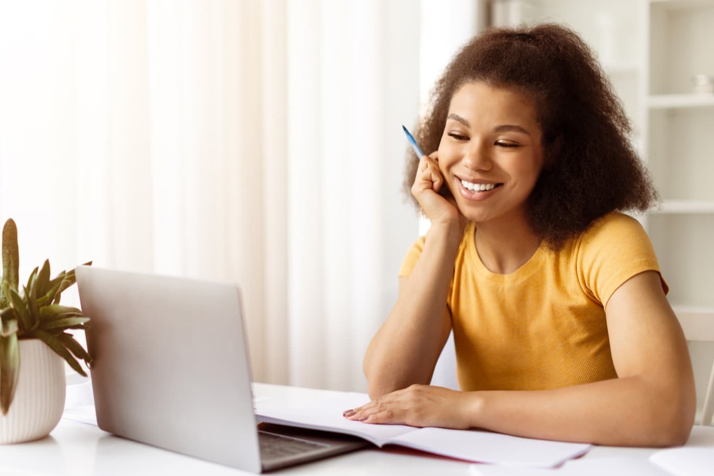 A student smiling at her laptop while working through her notes